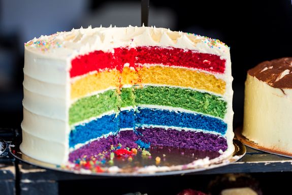 Angeschnittene Sahnetorte mit verschieden farbigen Böden in Regenbogenfarben